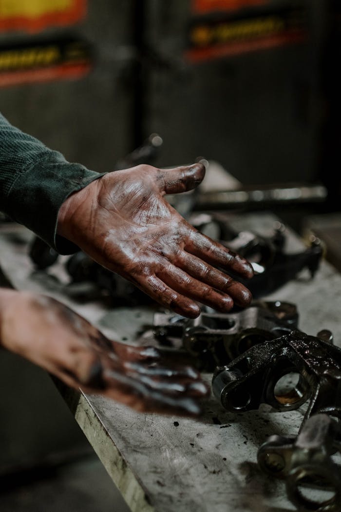 Close-up of a mechanics hands covered in grease while working on engine parts in a workshop.